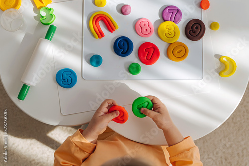 A little girl play with plasticine and creates colorful numbers. Learning to count through play. Early education. Fine motor skills, creativity and hobby.