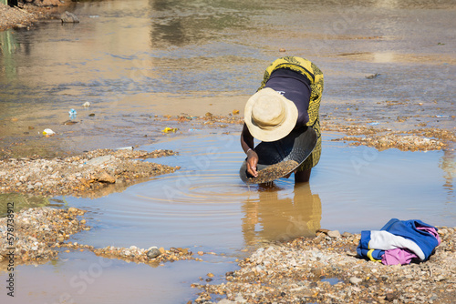 A woman panning for gold in Madagascar. Madagascar gold panner. A woman panning for gold in river. Reflection in water.  photo