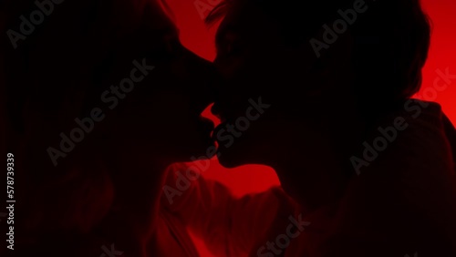 Studio portrait of enamoured couple in love hugging against red neon background
