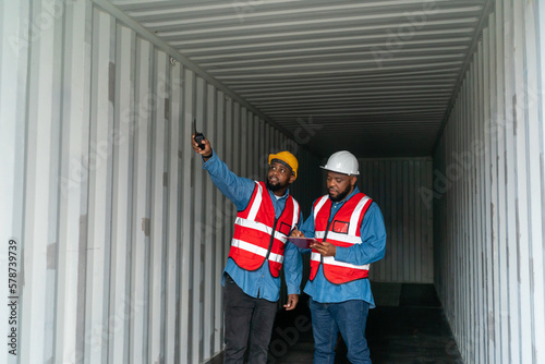 Portrait of Two African Engineer or foreman wears PPE checking container storage with cargo container background at sunset. Logistics global import or export shipping industrial concept.