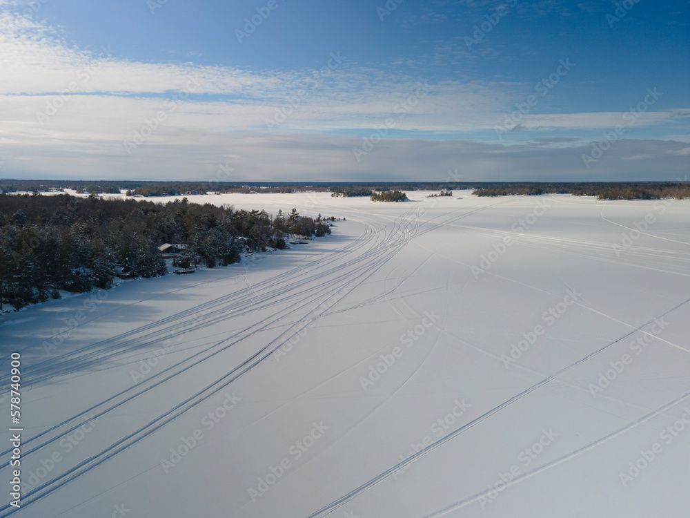 Winter scene - snowmobile tracks  on frozen lake covered with snow. Winter outdoor activities concept.