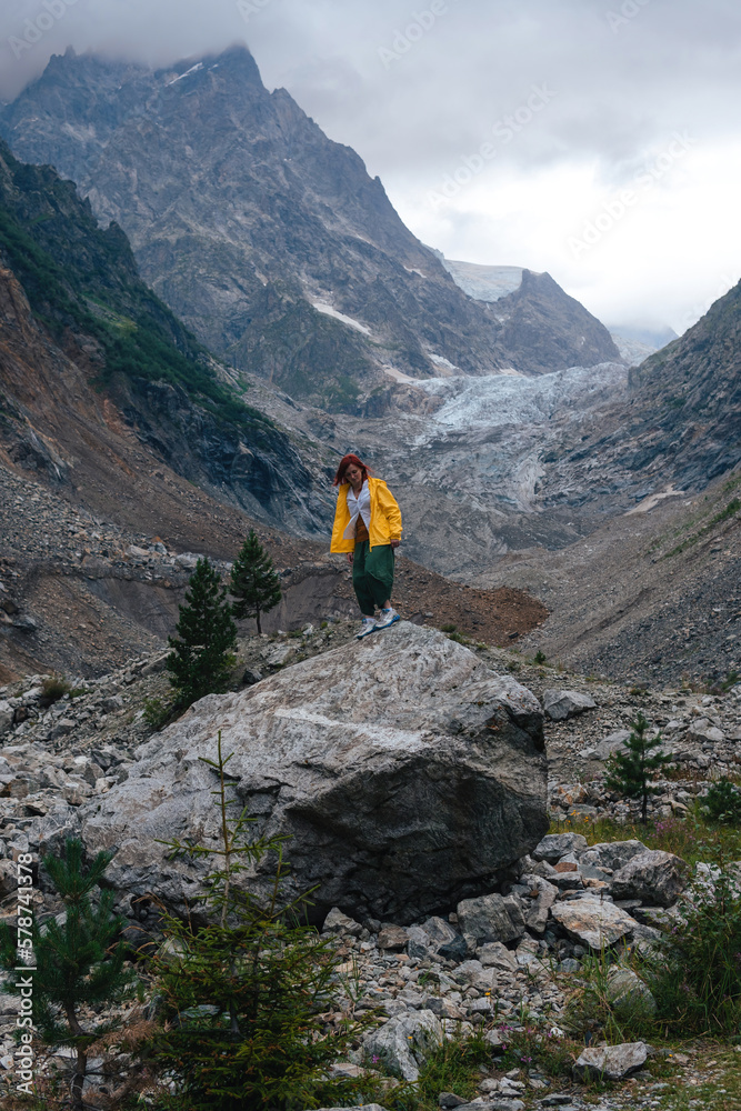 Traveling along mountains, freedom and active lifestyle, destination concept. Woman tourist in yellow jacket standing on mountain in Svaneti, Georgia near Chalaadi glacier hiking trail route
