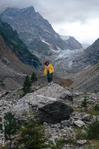 Traveling along mountains, freedom and active lifestyle, destination concept. Woman tourist in yellow jacket standing on mountain in Svaneti, Georgia near Chalaadi glacier hiking trail route