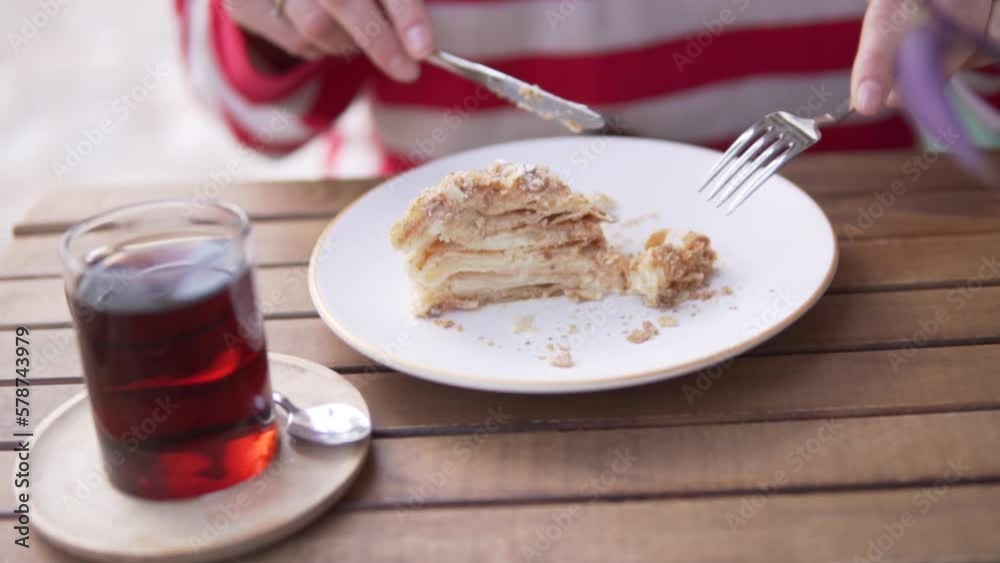 Close-up of a plate, a woman eating a honey cake with tea at a restaurant outside Close-up of a plate, a woman eating a honey cake with tea at a restaurant outside