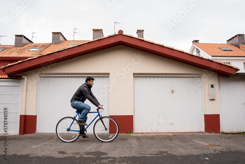 Man wearing jeans and black coat fixing a blue bike in front of garage