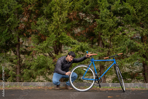 Man fixing a blue fixie bike wearing jeans and a black coat