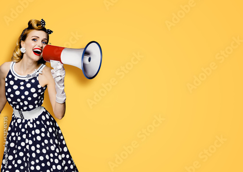Portrait image of beautiful woman holding mega phone, shout, saying, advertising. Pretty girl in black pin up style dress with megaphone loudspeaker. Isolated orange yellow background. Big sales ad.