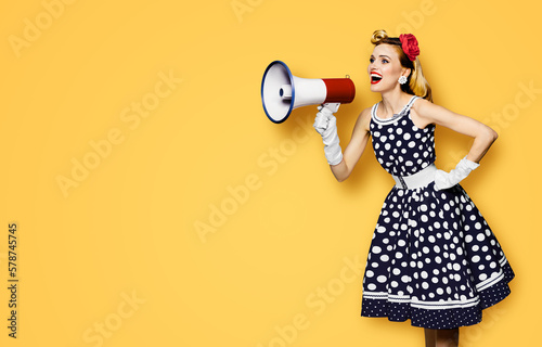 Portrait image of beautiful woman holding mega phone, shout advertising. Pretty girl in black pin up dress, white glows with megaphone loudspeaker. Isolated orange yellow background. Big sales ad.