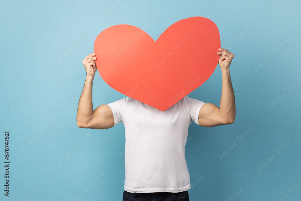 Man hiding behind big red paper heart, holding symbol of love care, cardiac issues. Man hiding behind big red paper heart, holding symbol of love care, cardiac issues.