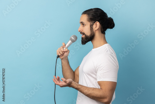 Side view of serious man wearing white T-shirt, journalist holding microphone, discussing problems.