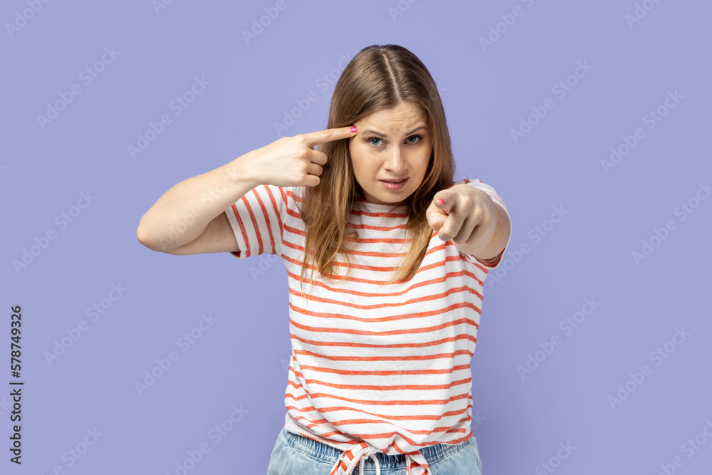 Woman holding finger near temple and pointing on you, showing stupid gesture, mocking. Woman holding finger near temple and pointing on you, showing stupid gesture, mocking.