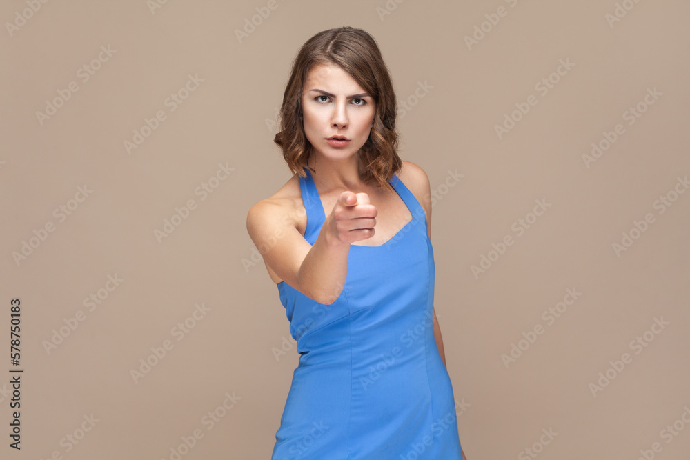 Strict bossy woman with wavy hair pointing at you, looking at camera with serious expression.