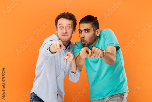 Comic men friends standing and pointing at camera, choosing you, having finny surprised expressions.