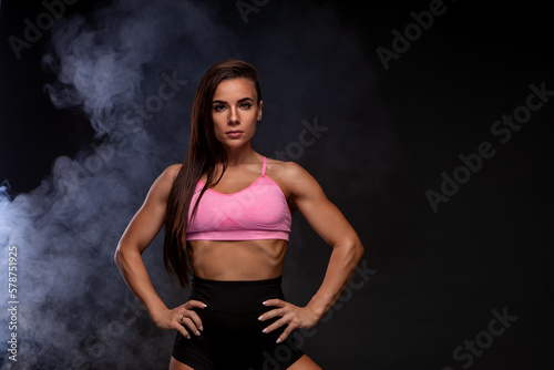 Beautiful athletic woman. Fitness girl in a sorted top and black shorts in smoke on a black background