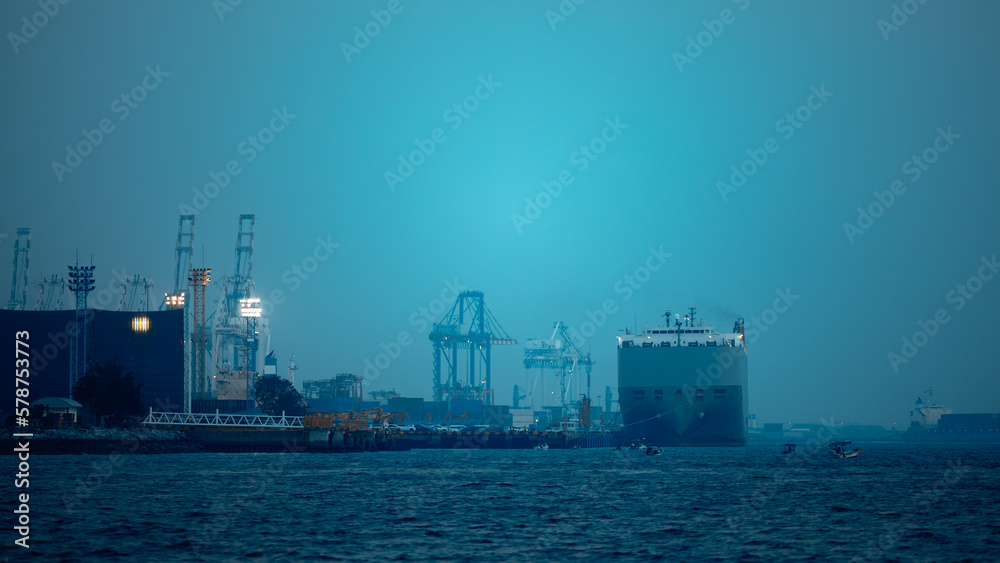 Large RoRo (Roll on/off) carrier vessels loading new cars and trucks at quayside into and out of the world market and commercial port, night scene blue tone process, sea front