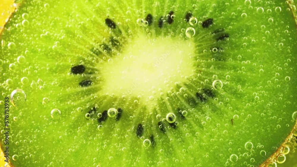 Ripe kiwi slices in air bubbles on an orange background.