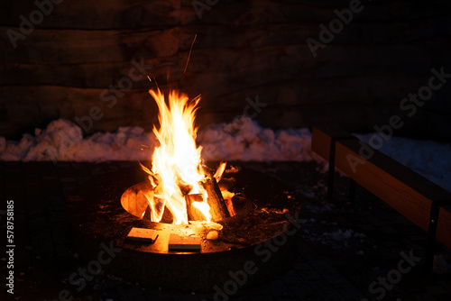 Firewood burns in the center of a round metal barbecue table.