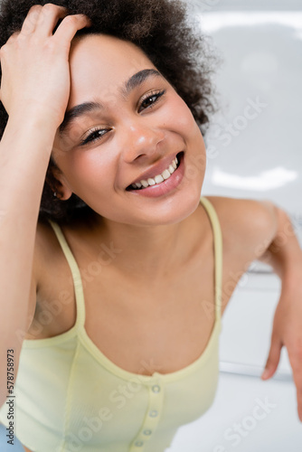 Portrait of positive african american woman sitting near blurred chair on grey background.