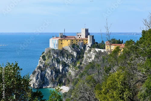 View of Castello di Duino on a cliff above the Adriatic sea in Friuli Venezia Giulia region of Italy with evergreen mediterranean vegetation