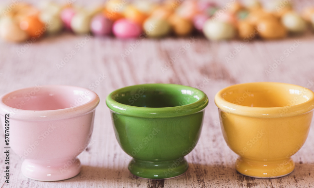 Three empty egg holders with small colored Easter eggs in the background Three empty egg holders with small colored Easter eggs in the background