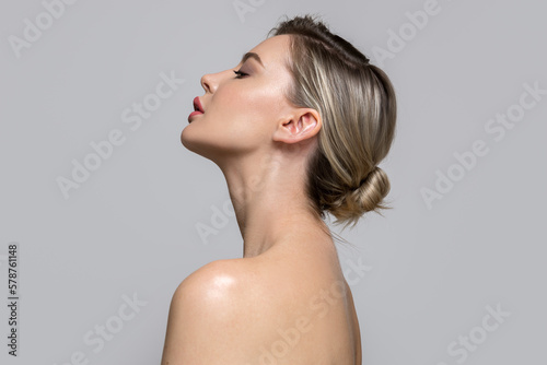 Young beautiful woman stands on her side with bare shoulders and back. Concept of hair and makeup, skin and body care photo