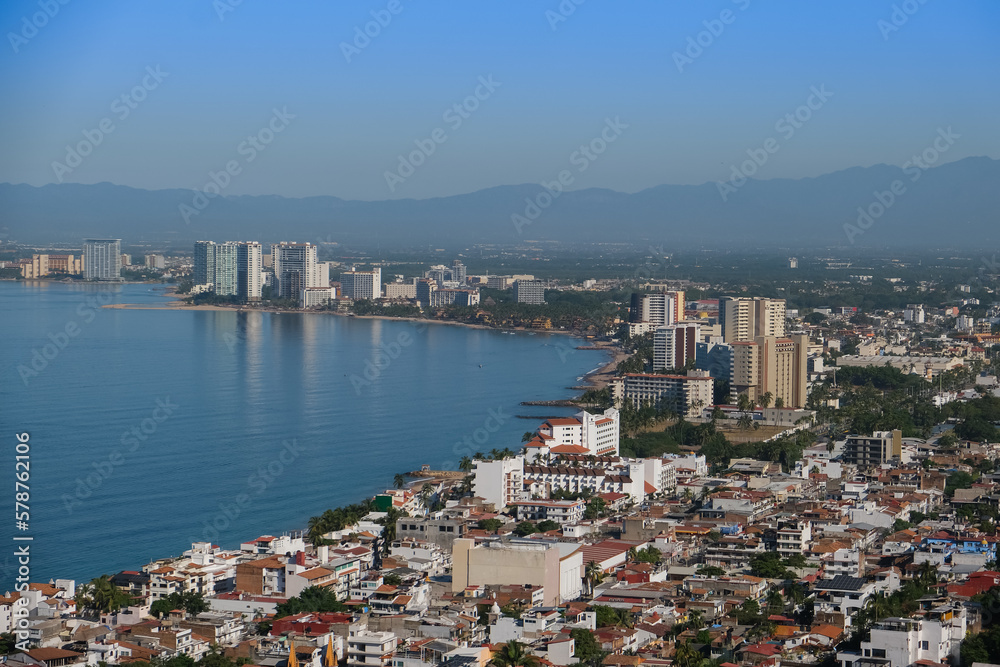 Aerial panoramic view of Puerta Vallarta city scape with white houses and clay shingled roofs and Bay of Banderas, sunny day, blue sky.