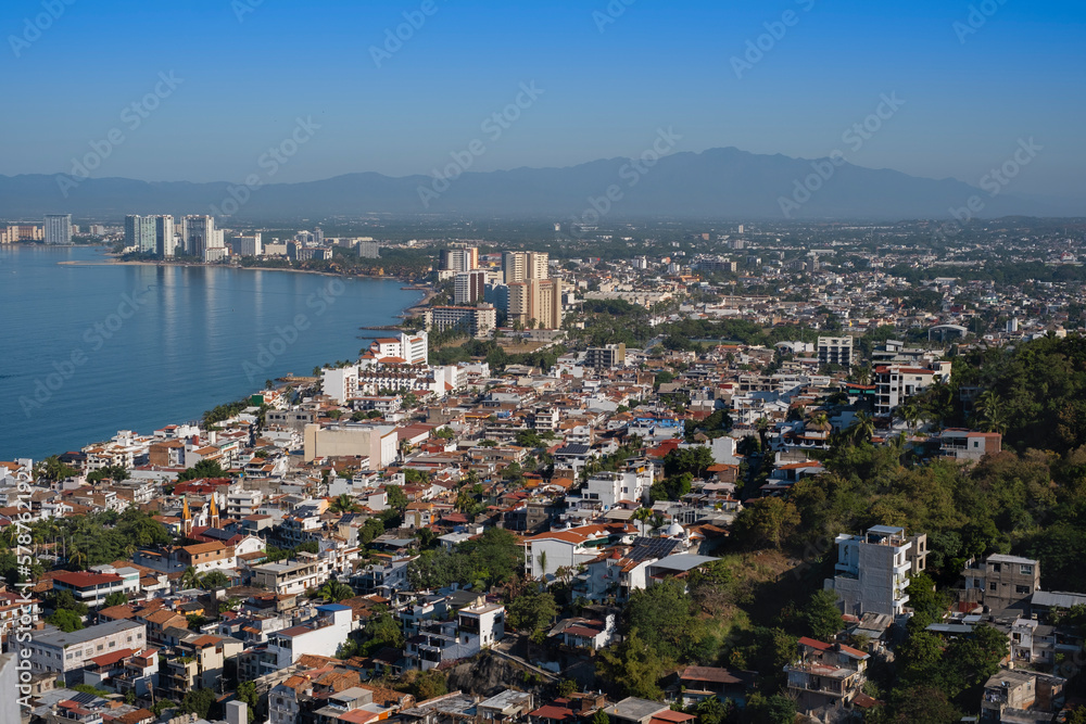 Aerial panoramic view of Puerta Vallarta city scape with white houses and clay shingled roofs and Bay of Banderas, sunny day, blue sky.