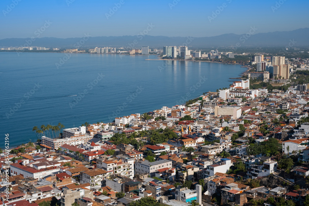 Aerial panoramic view of Puerta Vallarta city scape with white houses and clay shingled roofs and Bay of Banderas, sunny day, blue sky.