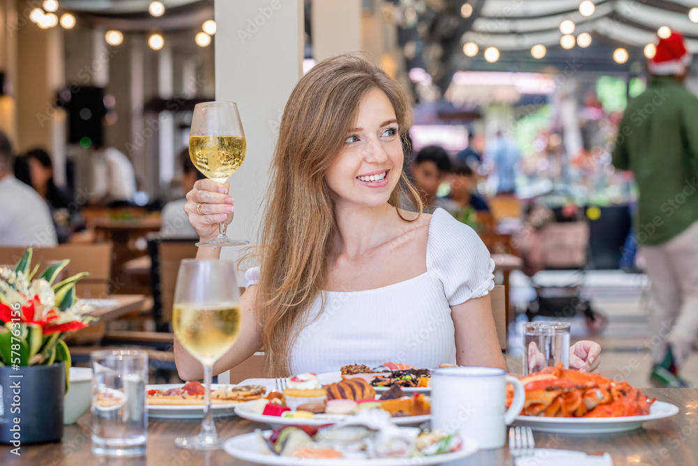 Woman indulging in fresh, delicious seafood and champagne at luxury restaurant. Walking waiters in the background. Brunch or lunch in a modern hotel or resort.