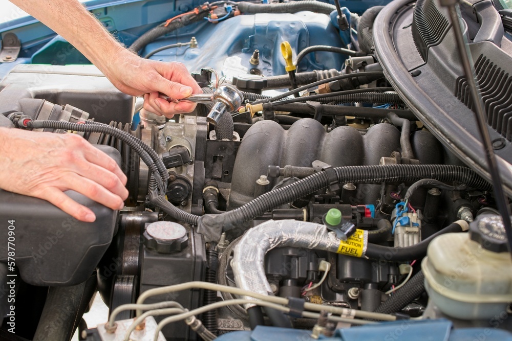 Automobile mechanic reaching into engine bay with socket wrench Automobile mechanic reaching into engine bay with socket wrench