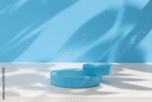 Pastel blue podium for products or cosmetics against bright blue background with leaves shadows.  