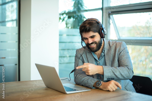 Canvas-taulu Smiling business man pointing finger right to the laptop screen talking on video call with client at office