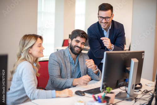 Group of three business people laughing together while looking at computer monitor and getting good company results. © Bojan