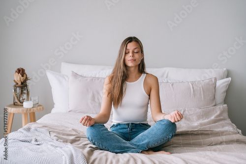 Photographie Focused young adult caucasian woman in white t-shirt sitting on bed in yoga meditation pose eyes closed