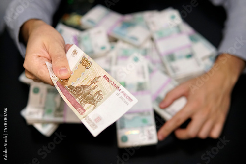 Leinwand Poster man holds out a hundred dollar bill in Russian rubles, holding hands of millions of rubles