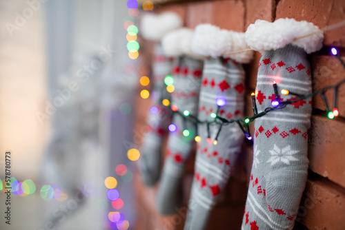 Gray Christmas socks on brick fireplace with colourful lights.