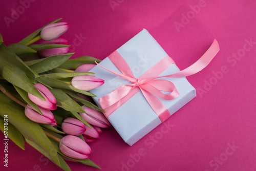 Romantic gift box tied with big pink bow and spring tulips on pink color background. Mother's day or Easter holiday concept. © Hanna Aibetova