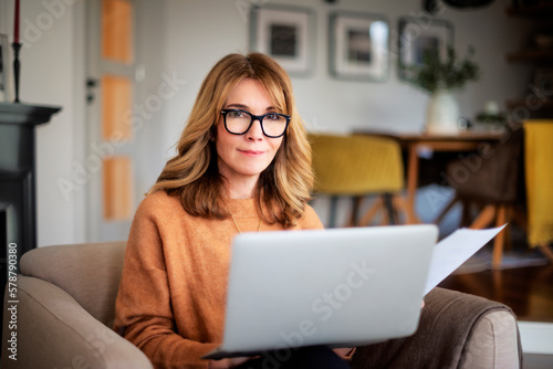 Mid aged woman sitting at home and using laptop for work
