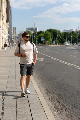 A man walks down a city street with a cup of coffee