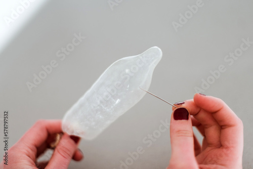 Una mano femenina pinchando con una aguja un preservativo de látex. Hacer un agujero en los preservativos para provocar el embarazo. Fallo del método anticonceptivo. 
