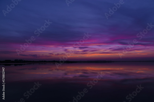 Scenic view of colorful sky reflected in the lake at evening, after sunset. Sunset at coast of the lake. Reflection, blue sky and yellow sunlight. Landscape during sunset. The beautiful nature around