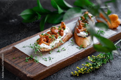 Two Bruschetta with chanterelles and Philadelphia cream cheese on a wooden board. Mushroom sandwich decorated with greens, selective focus