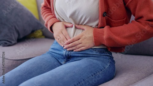 Stomach pain, cramps and woman hands on lounge with digestive and menstrual problem on a home couch. Constipation, tummy ache and abdomen health issue in a house on a sofa with bloating and ibs photo