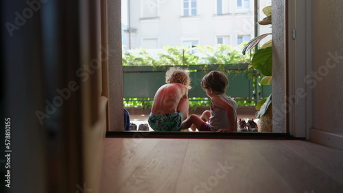 Φωτογραφία Children sitting by door step putting shoes on outside