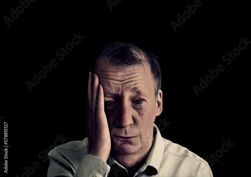 A depressed man holding his face with his hand, showing anguish. Medium closeup shot on black background. Generative AI.
 photo