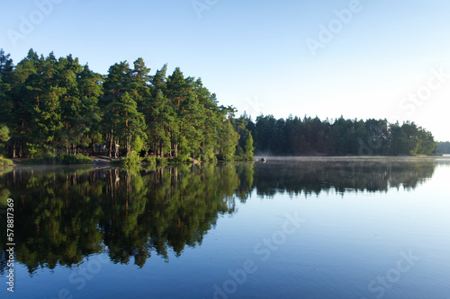 Sunny morning at a lake in Sweden with rising fog over water with forest in background