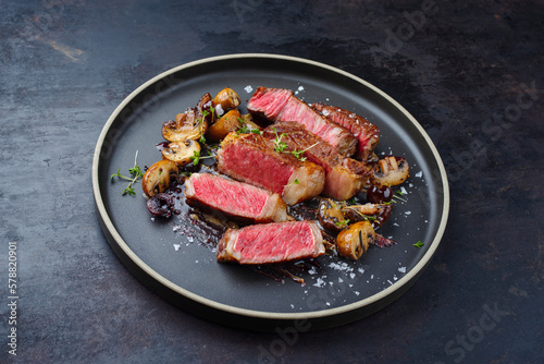 Modern style dry aged Wagyu rib eye beef steak with mushrooms in Amareno cherry and truffle sauce served as close-up on a Nordic design plate with text space