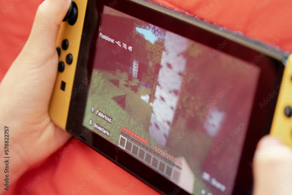 Fototapeta premium BARI, ITALY - OCTOBER 2, 2022: a kid playing with the Nintendo Switch gaming console, exploring the vast virtual world. Handheld closeup shot.