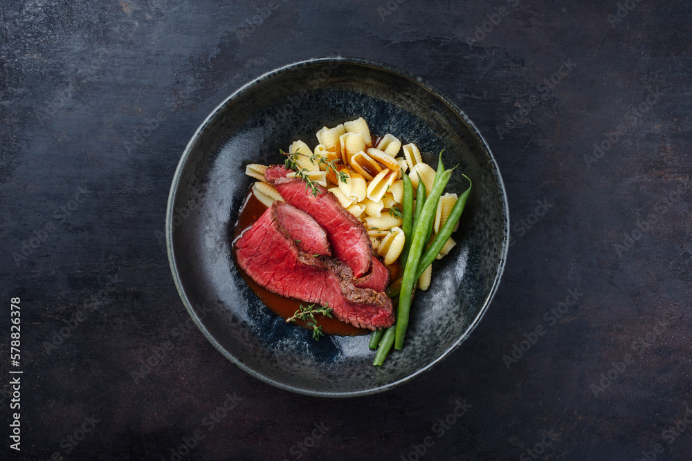 Traditional Italian chianina sliced roast beef with gnocchetti sardi pasta and beans in spicy red wine sauce served as top view in a Nordic design bowl with copy space