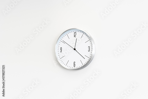 White clock hangs on the white wall. place for text, copy space.